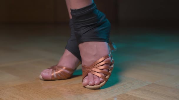 Latin dansı için dans ayakkabısı giymiş beyaz tenli ince bir kadının bacaklarının yakın çekimi. Karanlık bir odada durup bir rafta hareket ederler. Paralel kamera hareketi — Stok video
