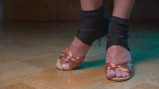 Primer plano de las piernas de una joven blanca delgada en zapatos de baile para bailar latino. En una habitación oscura se paran y se mueven en un estante. Movimiento paralelo de la cámara — Vídeo de stock