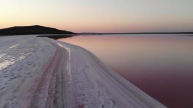 Akşam vakti pembe tuz gölünün tuzlu kıyılarında uçan hava manzarası, pembe suda mavi gökyüzü yansıması.