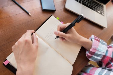 Masada mutfakta otururken not defterine not alan beyaz, çekici bir kadın. Kağıt defter kadın eli yazıyor.