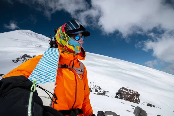 Ângulo largo tiro jovem alto esquiador profissional mantém seus esquis enquanto está de pé no alto das montanhas e olha para os picos cobertos de neve. — Fotografia de Stock