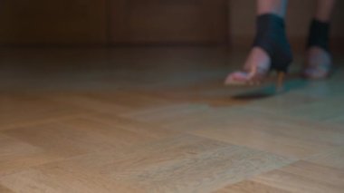 Balo salonu dansı için bej ayakkabılı kadın bacakları. Alçak topuklularla ve koruyucu kılıflarla. Fosforun karanlık bölgesinden ve birkaç sunum hareketinden çık
