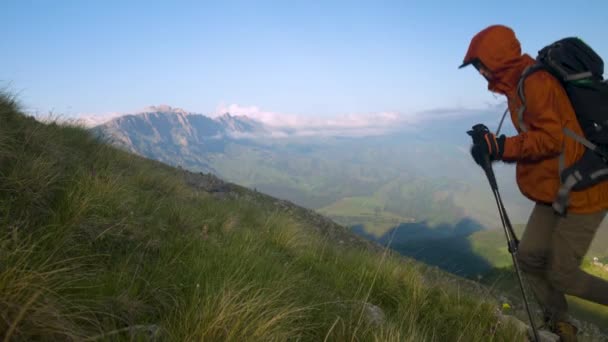 Mladá běloška turista s batohem a trekking tyče v čepicích a slunečních brýlích na letní večer procházky do kopce. — Stock video