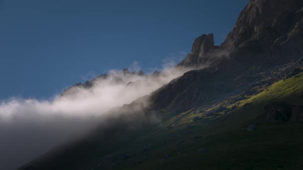 Sommer-Video-Landschaft niedrige Wolkendecke fließt um epische Klippen an einem Sommerabend bei Sonnenuntergang. Grüne Wiesen mit Gras am Fuße der felsigen Berge — Stockvideo