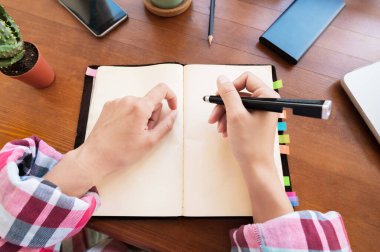 Masada mutfakta otururken not defterine not alan beyaz, çekici bir kadın. Kağıt defter kadın eli yazıyor.