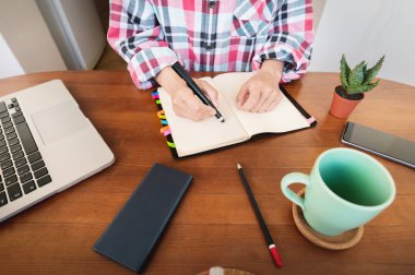 Masada mutfakta otururken not defterine not alan beyaz, çekici bir kadın. Kağıt defter kadın eli yazıyor.