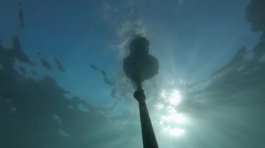 Açık deniz suyunda bir adam şnorkelle yüzüyor ve serbest dalış yapıyor. Bir dalgıcın silueti güneş ışınlarıyla derinlerde yüzüyor. Video içinde film tahılı