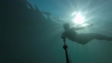 Açık deniz suyunda bir adam şnorkelle yüzüyor ve serbest dalış yapıyor. Bir dalgıcın silueti güneş ışınlarıyla derinlerde yüzüyor. Video içinde film tahılı