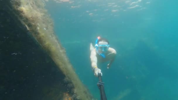 Un atletico caucasico con un bastone selfie si tuffa facendo snorkeling nell'acqua limpida del mare vicino al naufragio. Nave affondata coperta di alghe marine — Video Stock