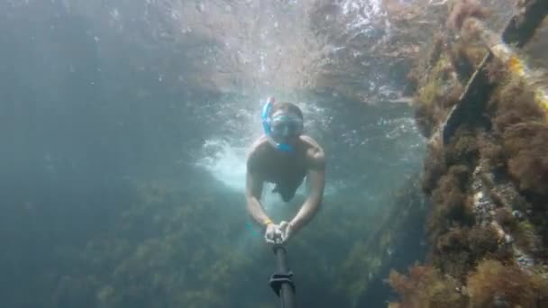 水中の沈没船の横にあるマスクで無料のダイビング若い男。自撮り棒アクションカメラ — ストック動画