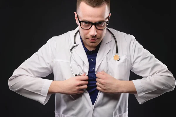 Jonge dokter een man met een bril en een badjas maakt een heldhaftig gebaar als een super man — Stockfoto