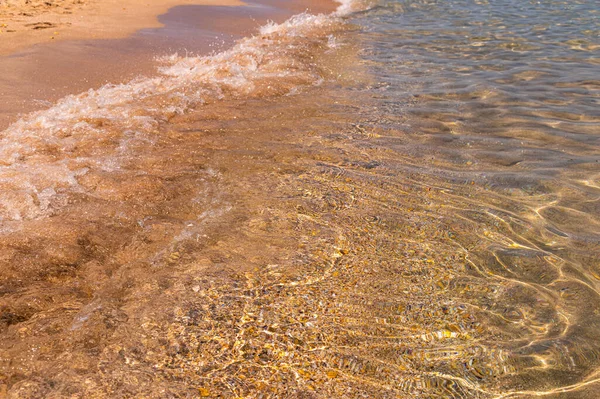 Tiszta tiszta víz a tengerben, napfény, hullámok és tengeri homok. Nyugodt tengervíz háttér — Stock Fotó