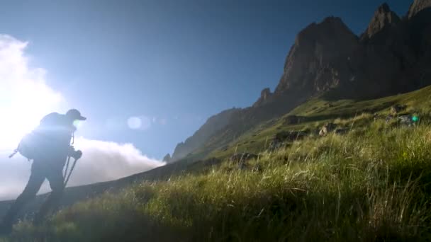 Turista mujer caucásica con una mochila y bastones de trekking en gorras y gafas de sol en una noche de verano camina por la colina. — Vídeos de Stock