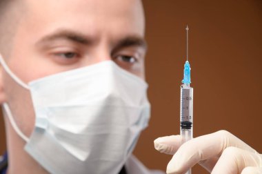 Close-up face of a caucasian doctor preparing a syringe for injection. Young male doctor in a protective mask and gloves holding a syringe with liquid.