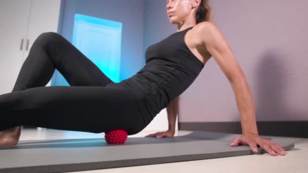 Sporty slim caucasian woman doing self massage on fitness mat with massage ball indoors. Self-isolation massage — Stock Video