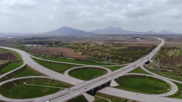 Widok z lotu ptaka na przedmieścia z kilkoma poruszającymi się pojazdami. Koncepcja podmiejskiej infrastruktury drogowej. Ciepły letni dzień na tle gór — Wideo stockowe