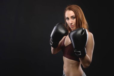 Spor giyim ve büyük siyah boks eldivenli beyaz kadın kameraya bakar ve yüzünü eldivenle kapatır. Boşluğu kopyala