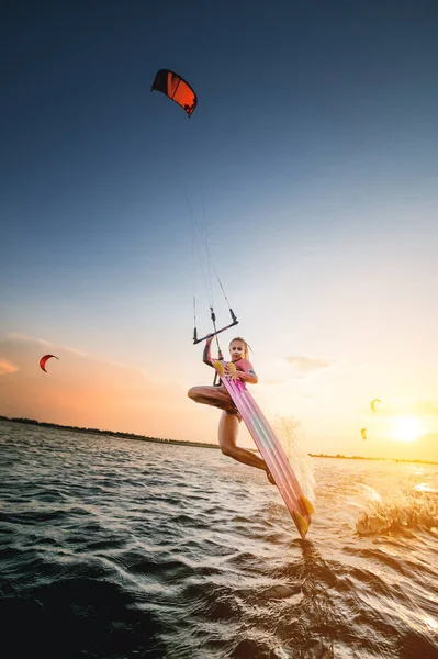 Wide angle. young caucasian woman in a wetsuit makes a trick sliding on the water against the backdrop of a sunset in the sea. Kitesurring girl athlete dark side trick on a kite with a board