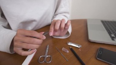 Evde tırnaklarını ve tırnaklarını keserek manikür yapan beyaz bir kadının yakın çekimi..