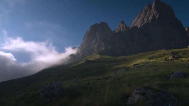 Широкий динамический диапазон панорамы скалистой горы с облаками, окруженными зеленой травой вечером перед закатом. Интенсивный кадр из сырого видео — стоковое видео