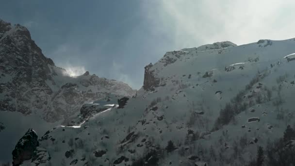 Der Wind bläst Schnee von der Klippe. Hohe schneebedeckte Berge an einem sonnigen Tag. Auszoomen — Stockvideo