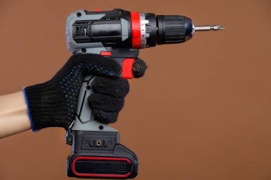 İş eldivenindeki bir kadın eli kahverengi arka planda bir tornavida tutuyor. Stüdyo çekimi