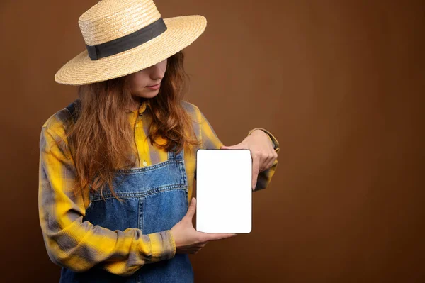 Długowłosy biały atrakcyjna młoda kobieta w wiejskiej odzieży, dżinsowe ogrodniczki i koszuli posiada elektroniczny tablet z ekranem wycięcia. — Zdjęcie stockowe