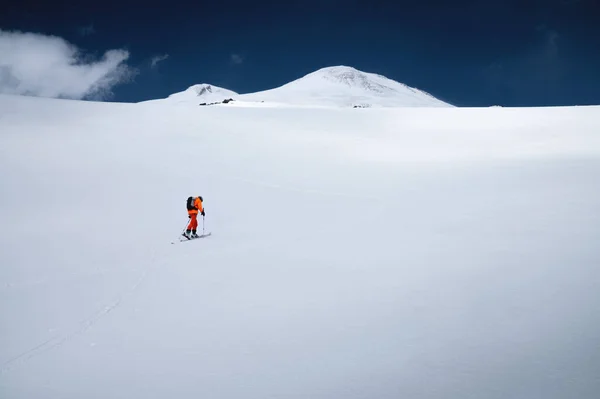 Mladý sportovec v oranžovém obleku vyleze na lyžařskou túru po zasněženém svahu k hoře Elbrus. Rozumím. Zimní horolezectví — Stock fotografie