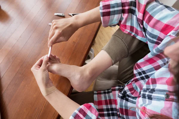 Gros plan d'une jeune femme à la maison en tenue décontractée assise à la table se faisant une pédicure dans la cuisine — Photo