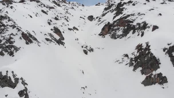 Neve coberto encosta rochosa selvagem no alto das montanhas. couloir íngreme para esqui extremo. Freeride spot para pilotos avançados. Vista aérea — Vídeo de Stock
