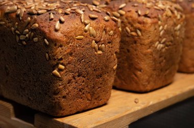 Tuğla şeklinde taze kahverengi çavdar ekmeği ve ekmek kabuğunda ayçiçeği çekirdeği. Tahta rafa uzan.
