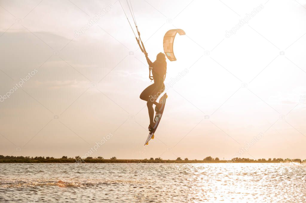 Young woman professional kiter performs a difficult trick in the air on a beautiful background of the sunset and sea