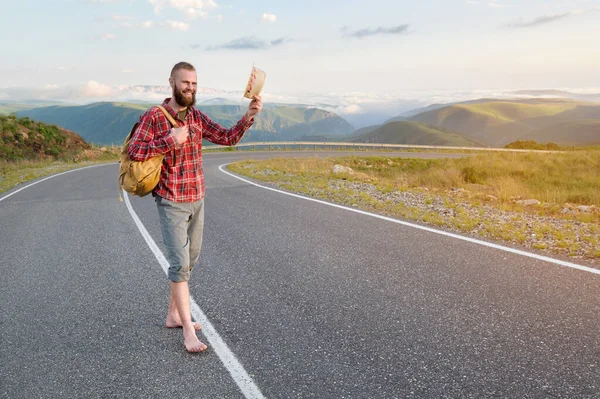 Sırt çantalı, tişörtlü, şortlu, güler yüzlü beyaz adam gün batımında dağların tepesinde bir kır yolunda dikilirken şapkasını kaldırarak seni selamlıyor.