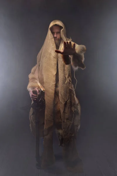 Hombre caucásico barbudo vestido como un antiguo monje mago con un bastón muestra un gesto de parada a la cámara y sonríe — Foto de Stock