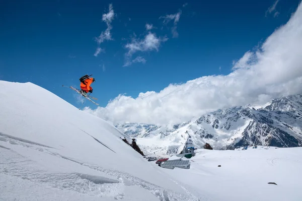 Atleta esquiador freestyle saltando em terno de esqui laranja em montanhas nevadas em um dia ensolarado — Fotografia de Stock