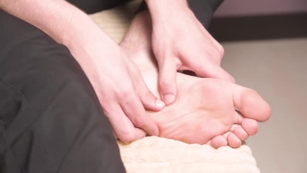 Kafkasyalı genç adam ayak masajı yapıyor. Profesyonel bir masör, ayak yüzeyine doğru masaj uygulamasını gösterir. — Stok video