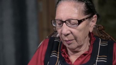 Yaşlı, çekici, üzgün, gözlüklü yaşlı kadın. Odada bir sandalyede otururken hapları elinde tutuyor.