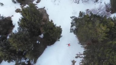 Turuncu takım elbiseli bir kayakçının havadan görünüşü bir bahar ormanındaki kar kalıntıları arasında geziniyor. Baharda ekstrem kayak
