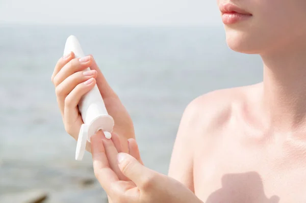 Young caucasian woman puts sunscreen on hand on the background of the sea on a sunny day — Stock Photo, Image