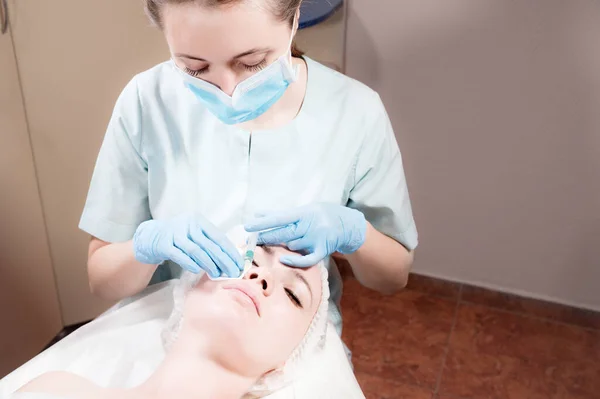 Молодая кавказская девушка получает инъекцию ботокса в щеку от профессионального косметолога в салоне красоты — стоковое фото