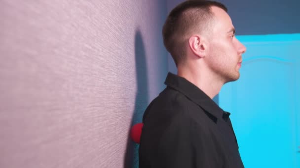 Närbild av en ung vit man som gör myofascial självmassage med en massageboll mot väggen. 4k upplösning — Stockvideo