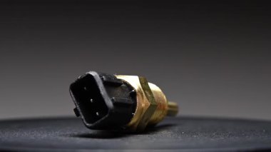 Yedek parça. Yeni motor soğutucu sıcaklık sensörü. Gradyan arkaplanda yeni bir parça döndürülüyor. Sığ alan derinliği