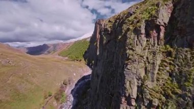 FPV insansız hava aracı keskin dağ uçurumları üzerinde uçuyor. Dağlara düşen bir uçurumun havadan görünüşü. Kayalık dalış