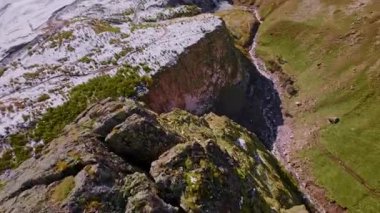 FPV insansız hava aracı keskin dağ uçurumları üzerinde uçuyor. Dağlara düşen bir uçurumun havadan görünüşü. Kayalık dalış