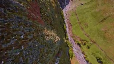 FPV insansız hava aracı keskin dağ uçurumları üzerinde uçuyor. Dağlara düşen bir uçurumun havadan görünüşü. Kayalık dalış