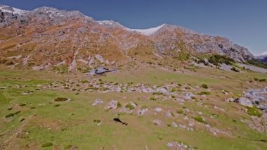 Dağlardaki gri bir helikopterin hava görüntüsü. Yeşil dağlarda teknik ulaşım uçuşları gerçekleştiriyor. Dağlarda kargo taşımacılığı. Sivil Havacılık