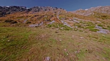 Dik, kayalık bir dağ tırmanışının ve güneşli bir günde güzel, taşlı bir yamacın hızlı ve aşırı yakın çekimi. Bir FPV İHA düzgünce ve hızla yamaca doğru uçar.