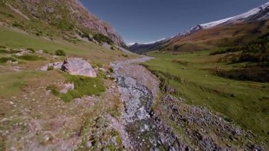 Güneşli bir günde kayalık bir vadide hızla akan bir nehrin nefes kesici alçak irtifa FPV drone görüntüsü.