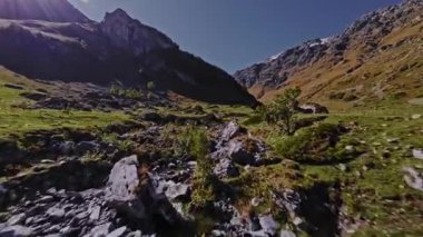 Güneşli bir günde kayalık bir vadide hızla akan bir nehrin nefes kesici alçak irtifa FPV drone görüntüsü.