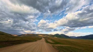 Yüksek hızlı güneşli bir günde toprak yolda araba sürmek. Yollar bozkırlardan ufuktaki dağlara kadar uzanıyor. Arabanın içinden ilk kişi göründü.
